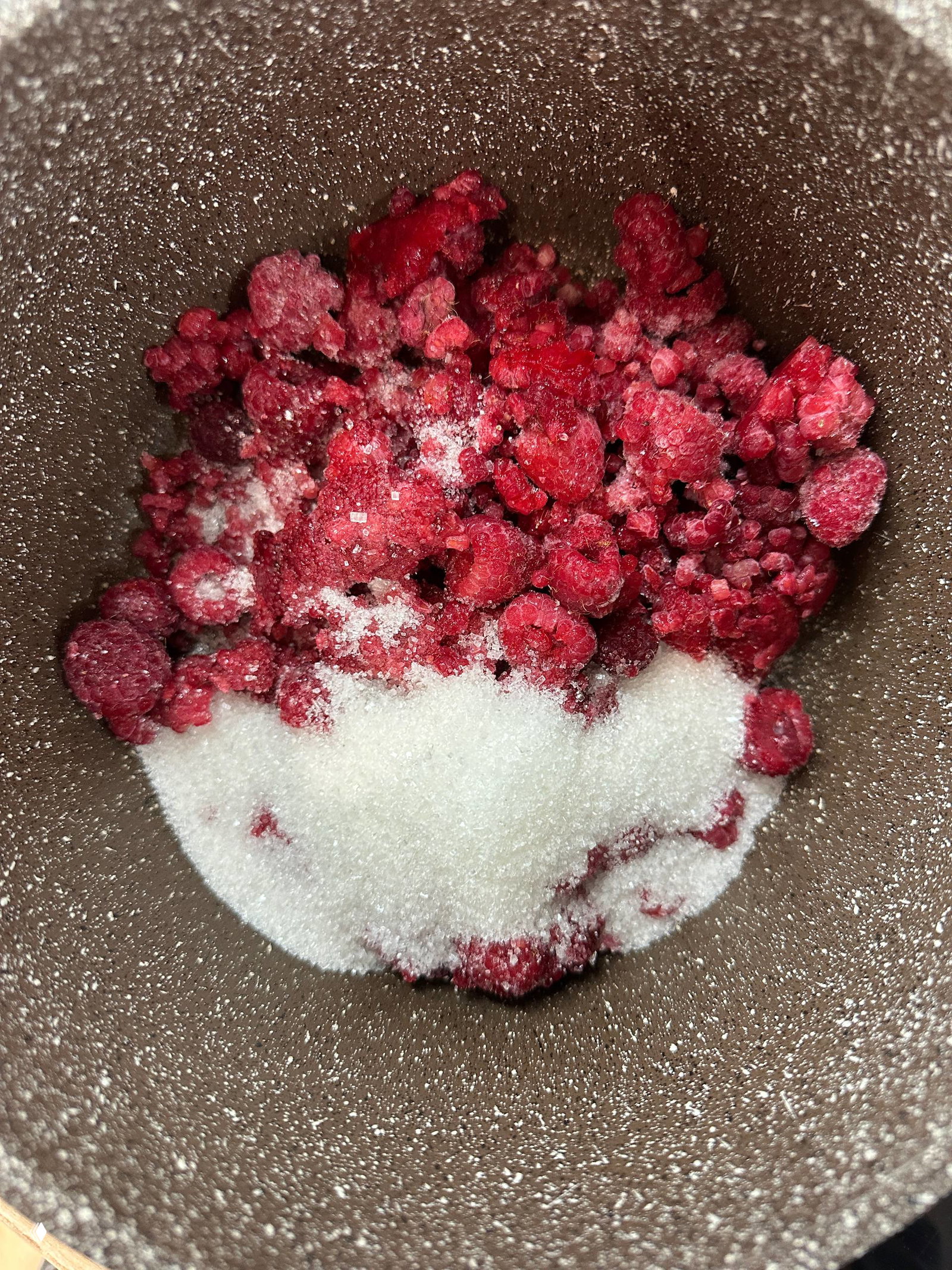 Крупный план замороженной малины с сахаром в сотейнике; яркие ягоды перед увариванием для малиновой начинки и получения нужной текстуры.