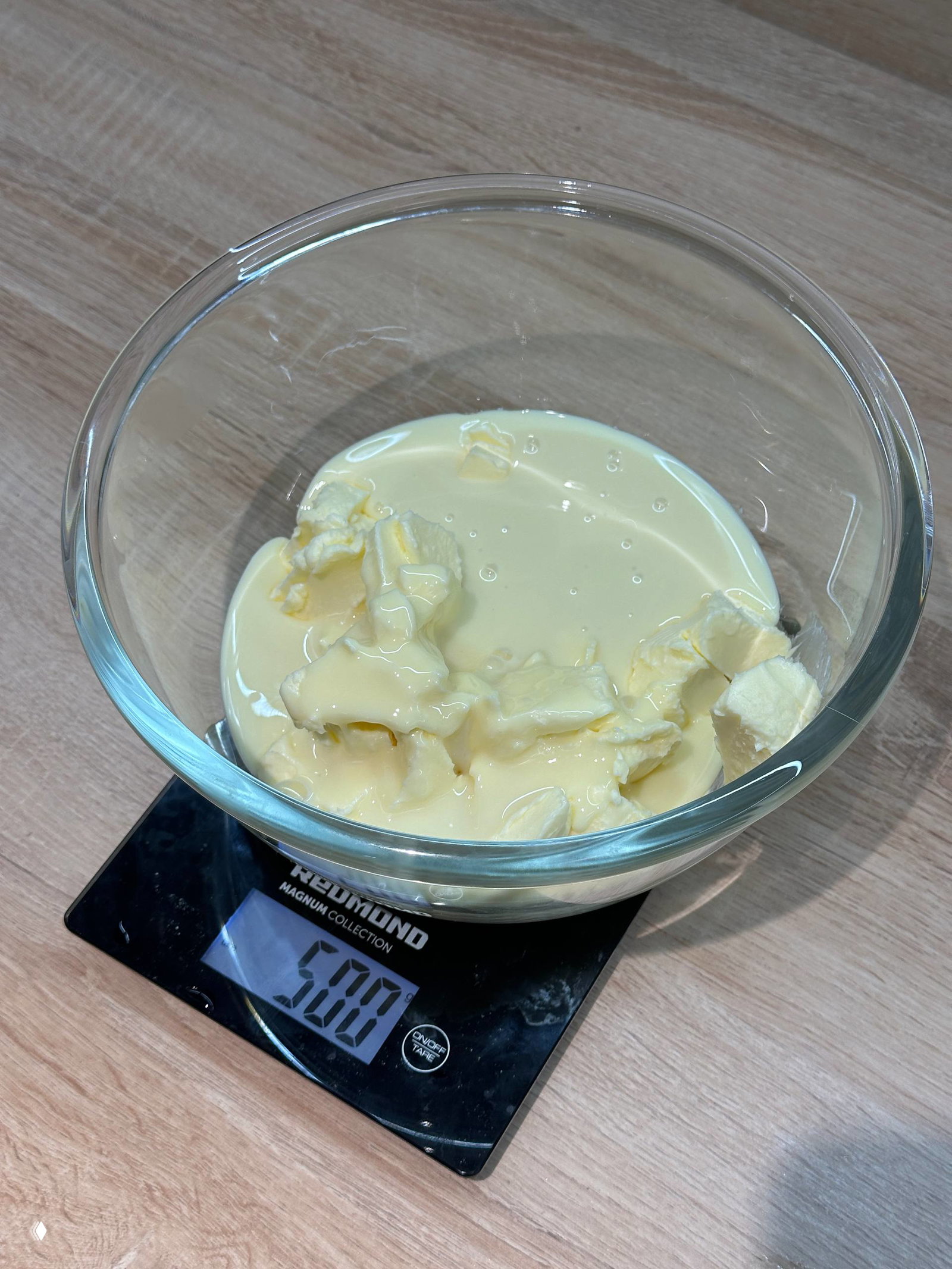 Стеклянная миска со сливочным маслом и сгущёнкой на кухонных весах; подготовка ингредиентов для крема Наполеона перед взбиванием.