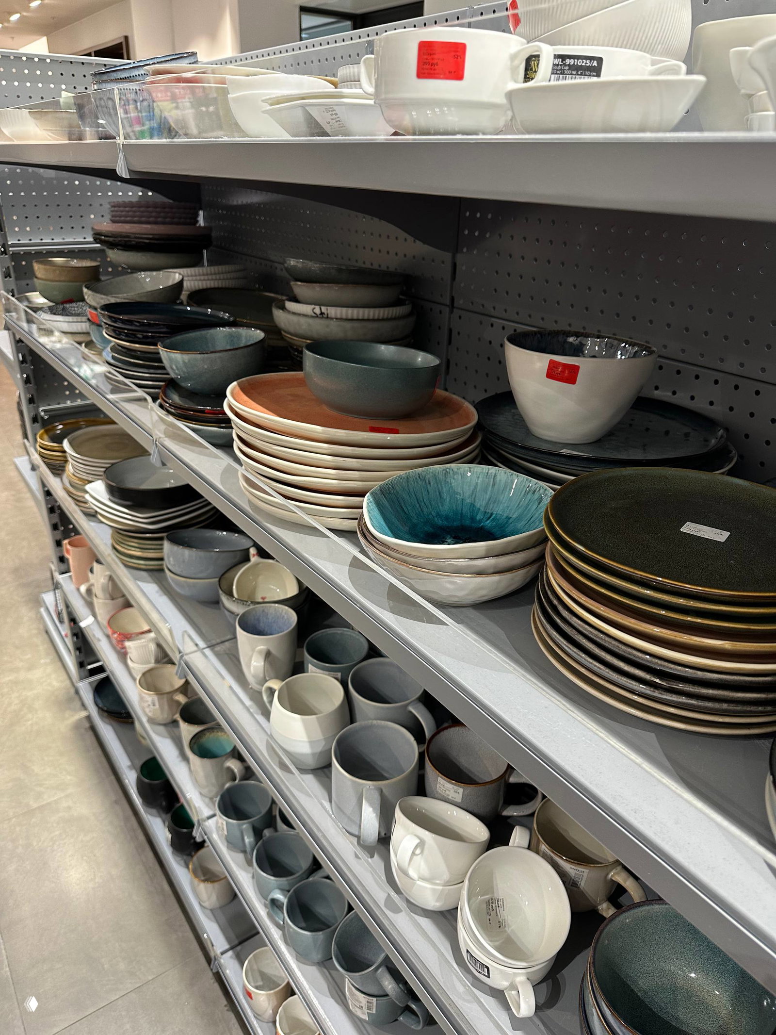 Стеллаж с тарелками, мисками и кружками разных форм и оттенков — нейтральная и монохромная керамика, часть ассортимента Offprice.