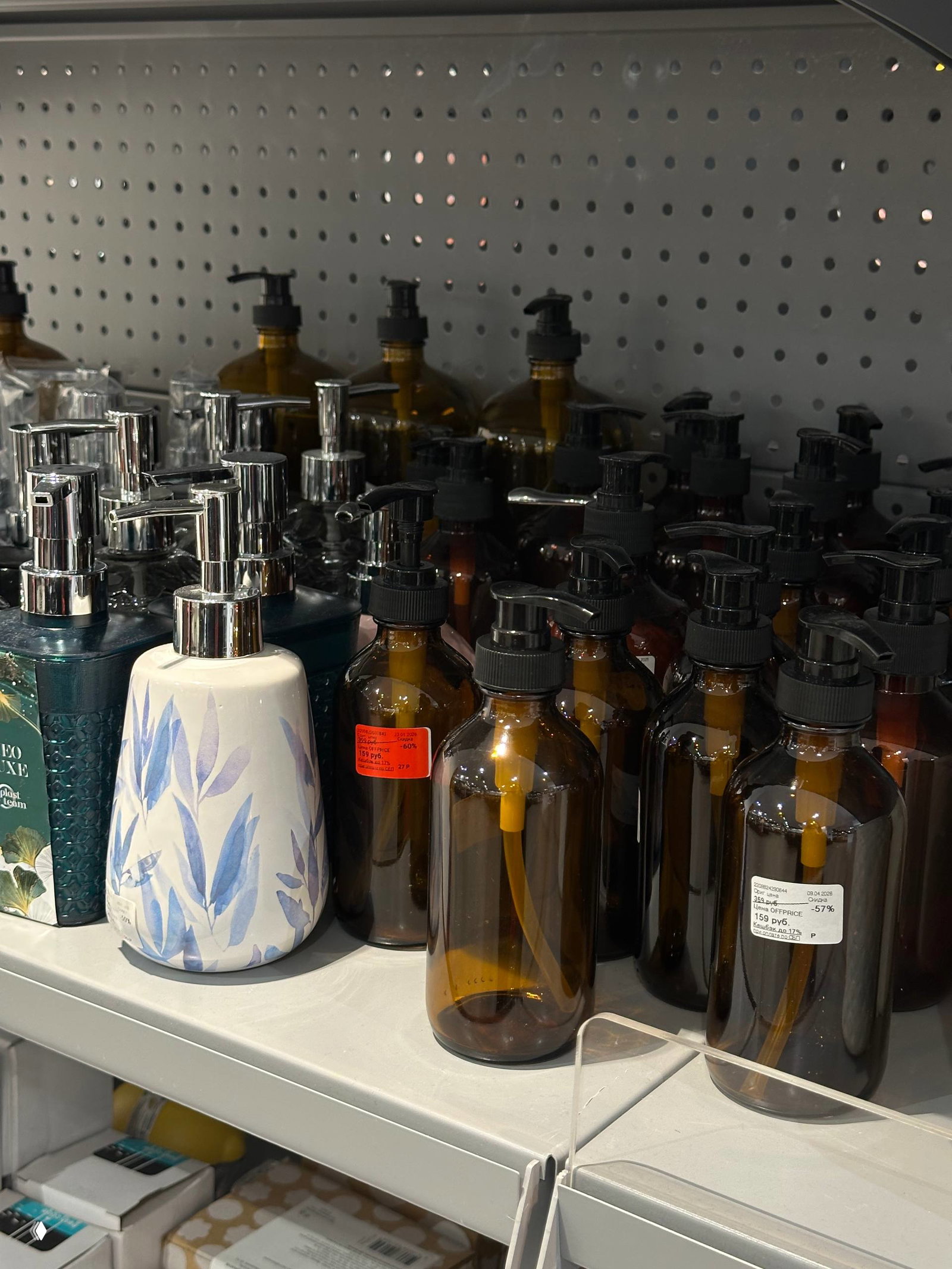 Бутылочки-дозаторы и флаконы для косметики и мыла в тёмном стекле, выставленные на полке магазина с стикерами скидок Offprice.
