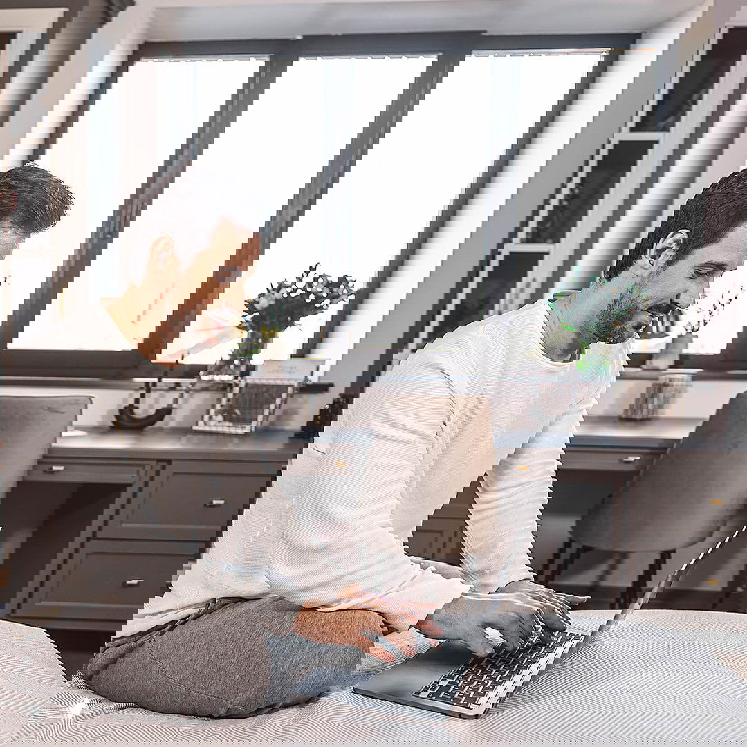 Мужчина с ноутбуком у большого окна в домашней обстановке — демонстрация комфорта и доверия к профессиональным решениям по окнам.