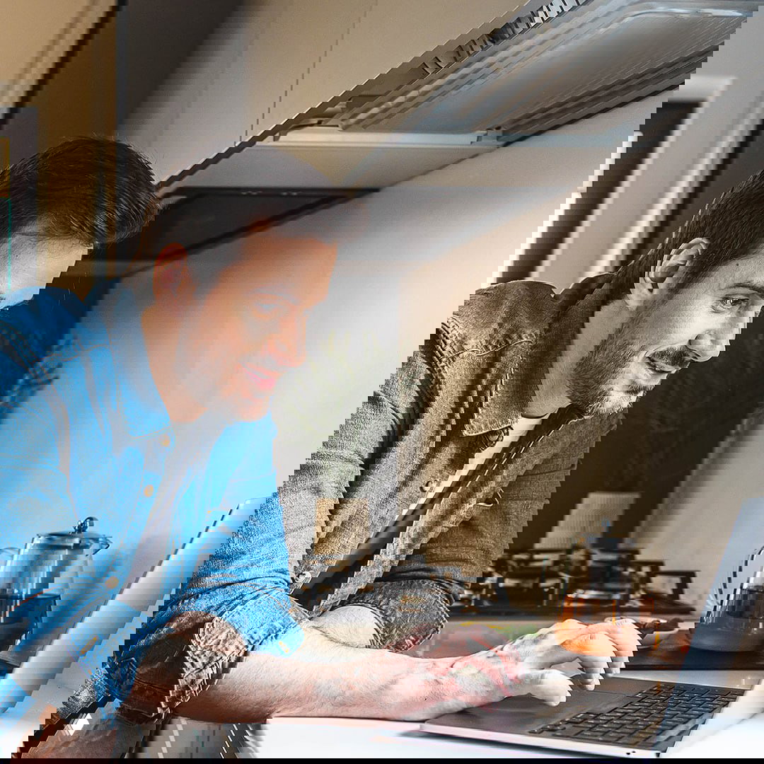 Фотография мужчины за ноутбуком на кухне — образ пользователя, читающего обзоры и инструкции по выбору продукции РЕХАУ в интернете.