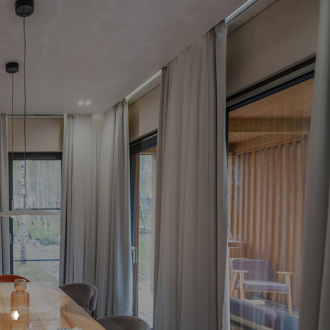 Столовая зона с большими окнами в тёмной раме и лёгкими шторами; интерьер с природным видом за окном и спокойной палитрой.