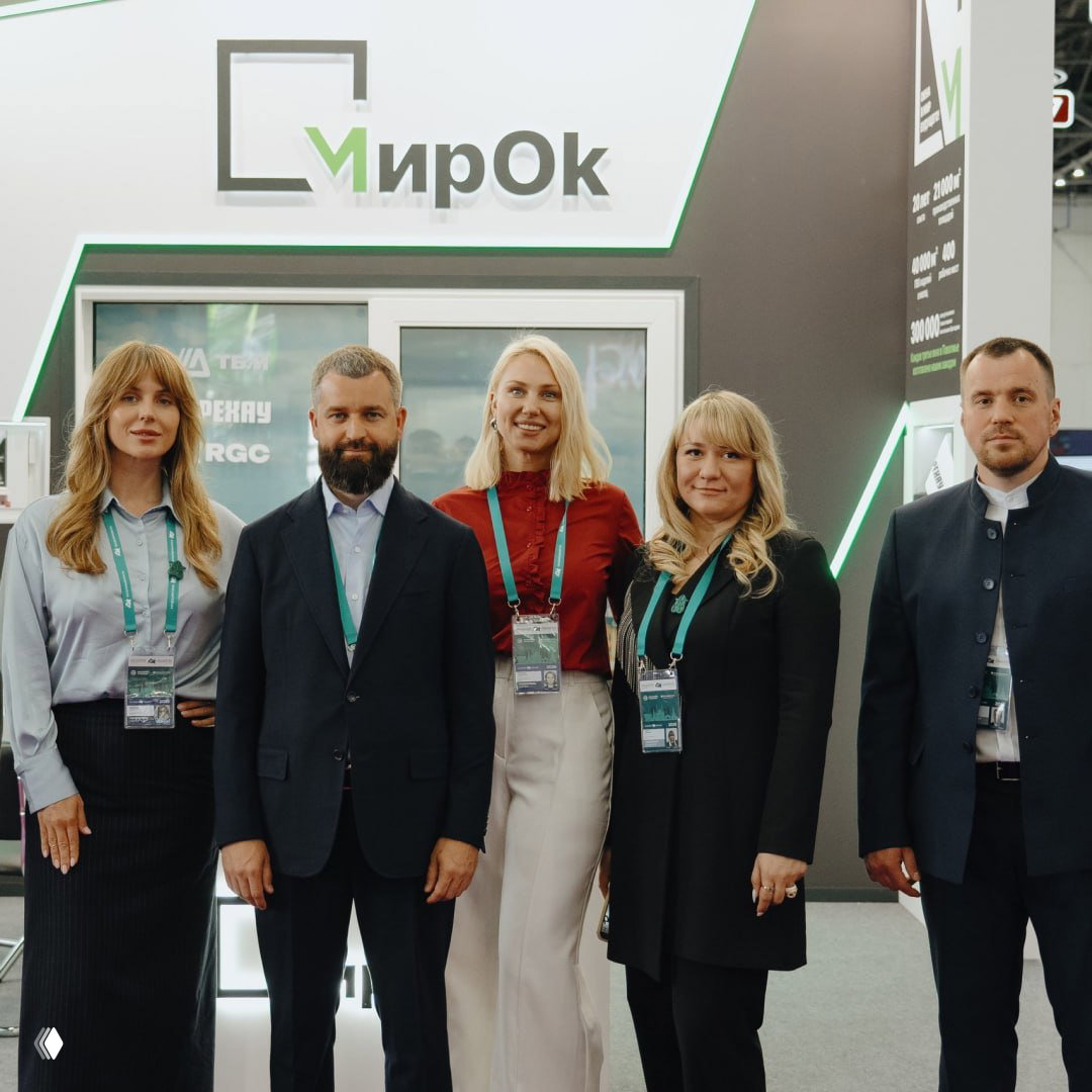 Фото команды на фоне логотипа «МирОк»: группа сотрудников и партнёров на выставочном стенде, корпоративная фотография в деловом стиле.