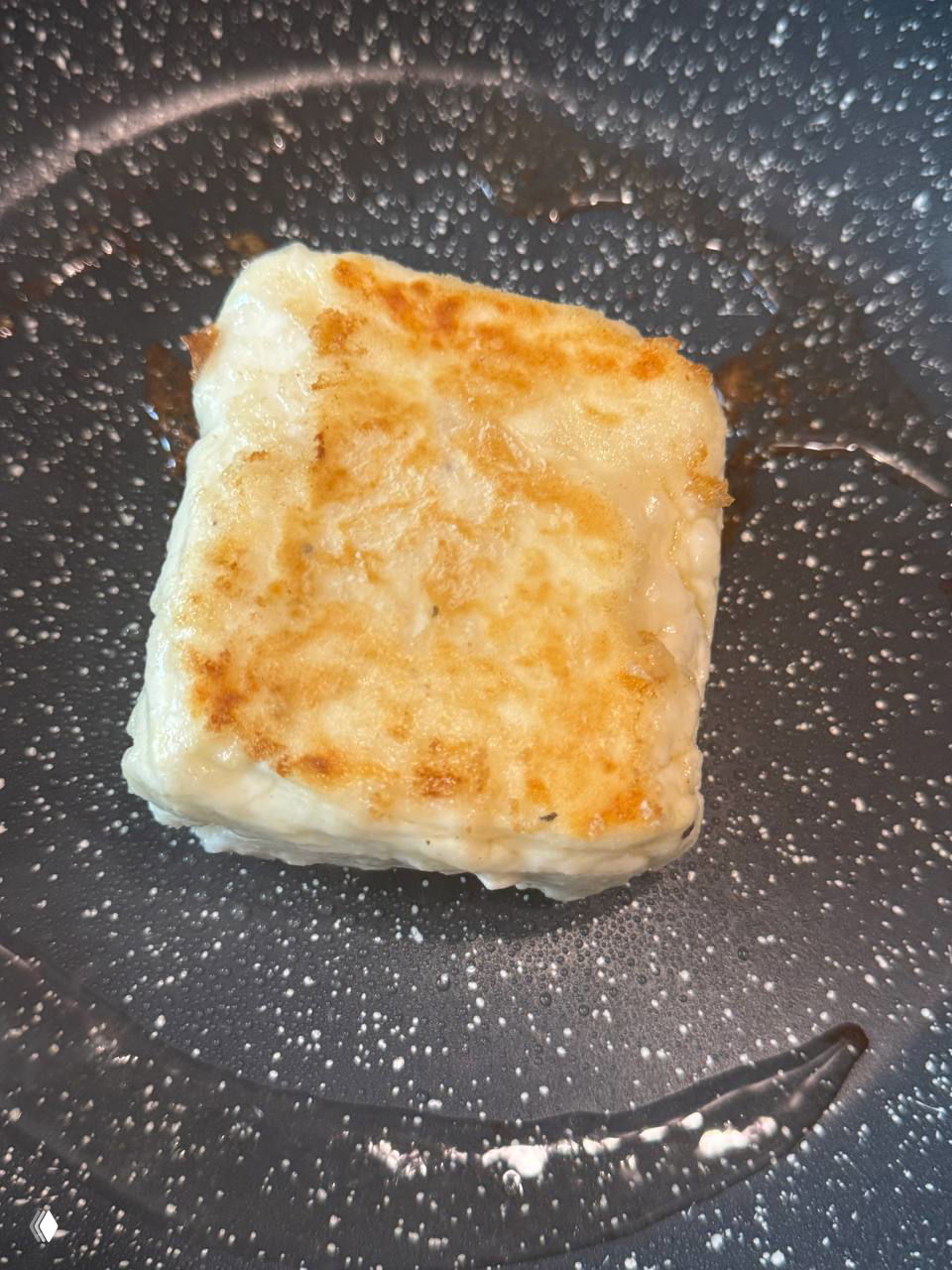 Кусок жареного халуми на сковороде с золотистой корочкой, вид сверху — демонстрация текстуры и неплавления сыра при жарке.