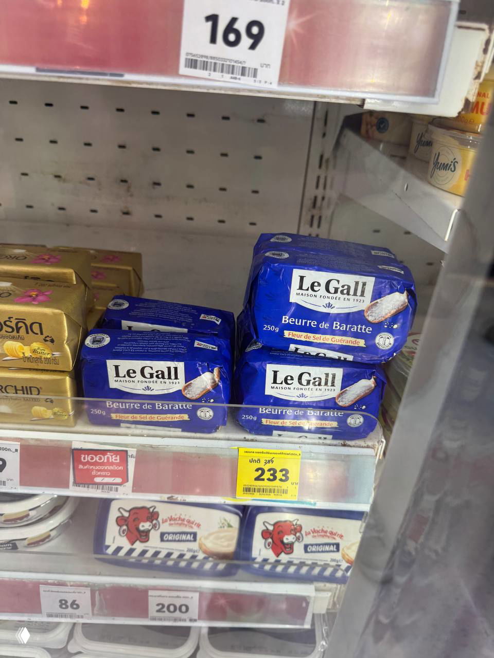Полка супермаркета Lotus с несколькими синими пачками масла Le Gall Beurre de Baratte и заметным ценником 233 бата; видны другие молочные товары вокруг.
