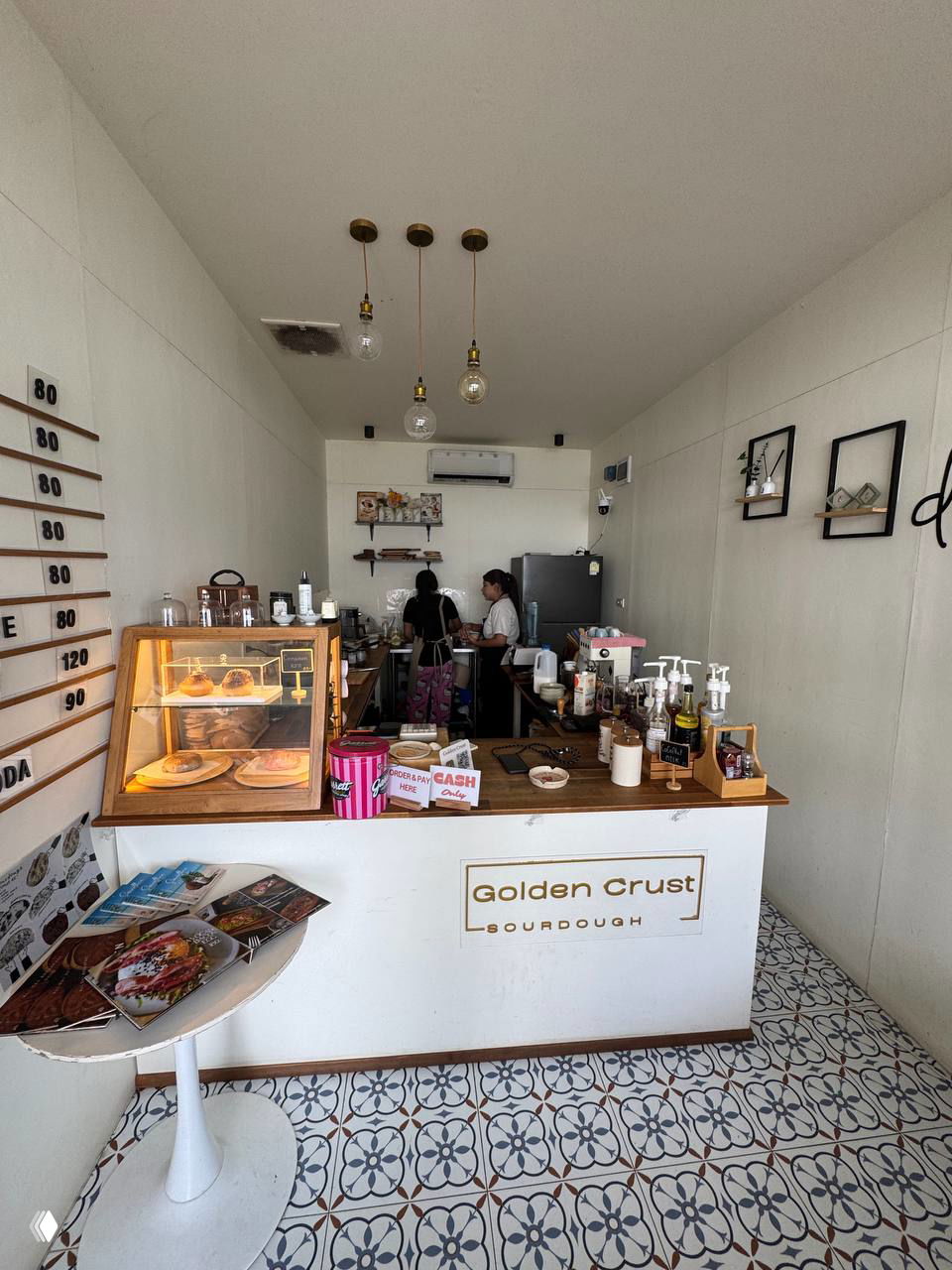 Интерьер маленького кафе Golden Crust: прилавок, витрина с выпечкой, две девушки за стойкой и кофейное оборудование.