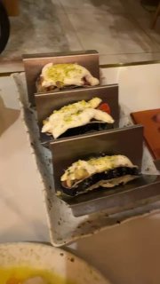 Три аккуратно выложенных тако с темпурой из баклажана в металлической подставке на столе: текстура, подача и соус видны крупным планом.