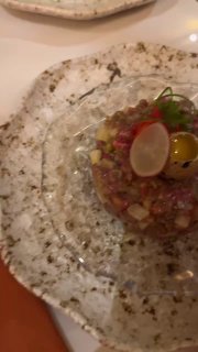 Крупный план биф тартар на мраморной тарелке: мелко нарезанное мясо, аккуратная подача, дольки редиса и оформление в жаркой атмосфере ресторана.