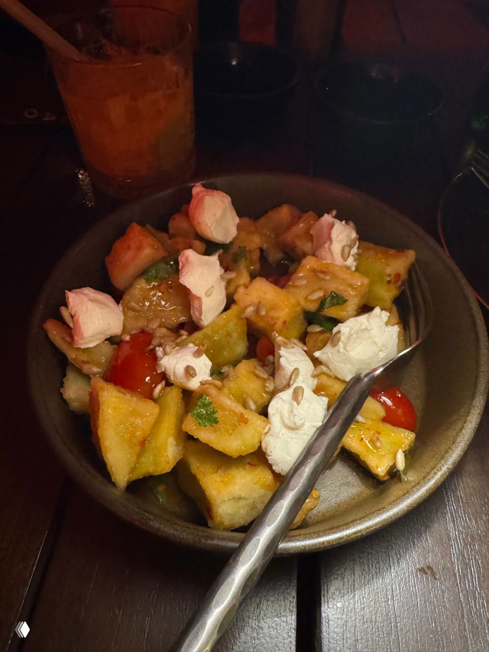 Миска с хрустящими баклажанами, черри, семечками и нежными ложками творога — салат подан в тёмной керамике, кадр при мягком освещении.