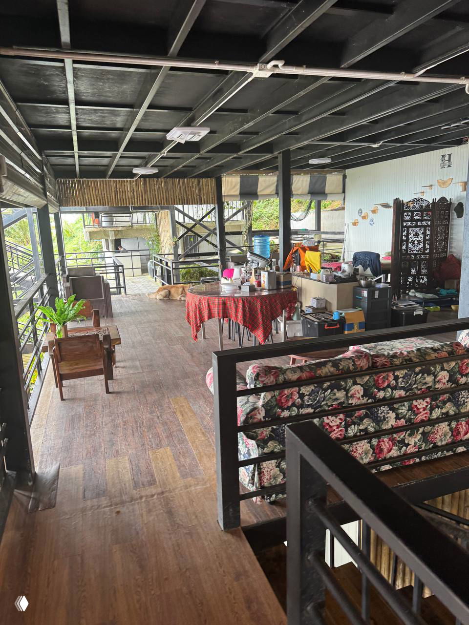 Интерьер открытой веранды Highland Paradise: деревянный пол, столы, диваны в цветочный принт и рабочие зоны на фоне склона — видна организация пространства.