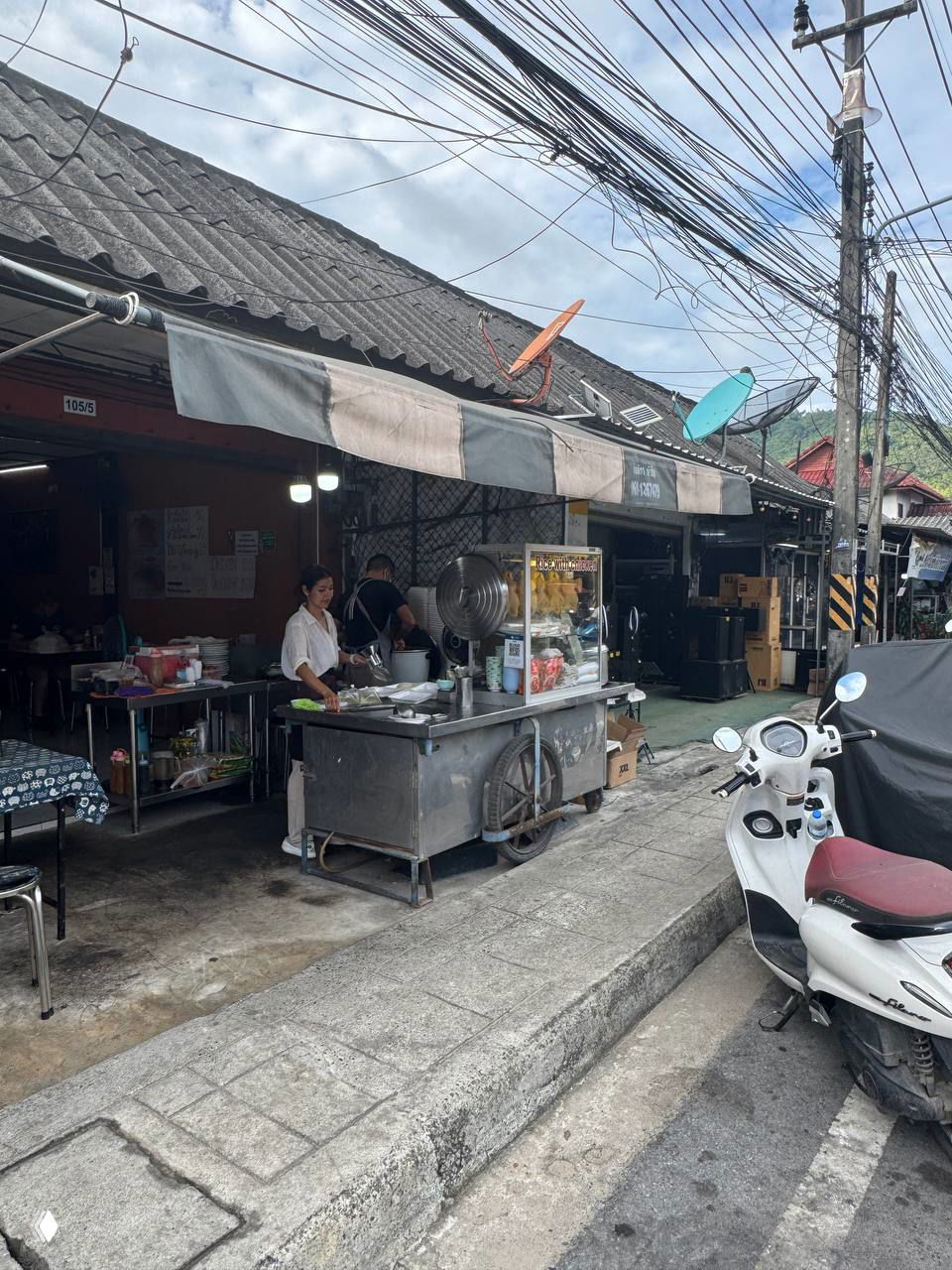 Уличный закуток на Ламай с тележкой и столиками, фасадом лавки и припаркованным скутером — типичный формат простого тайского кафе у дороги.