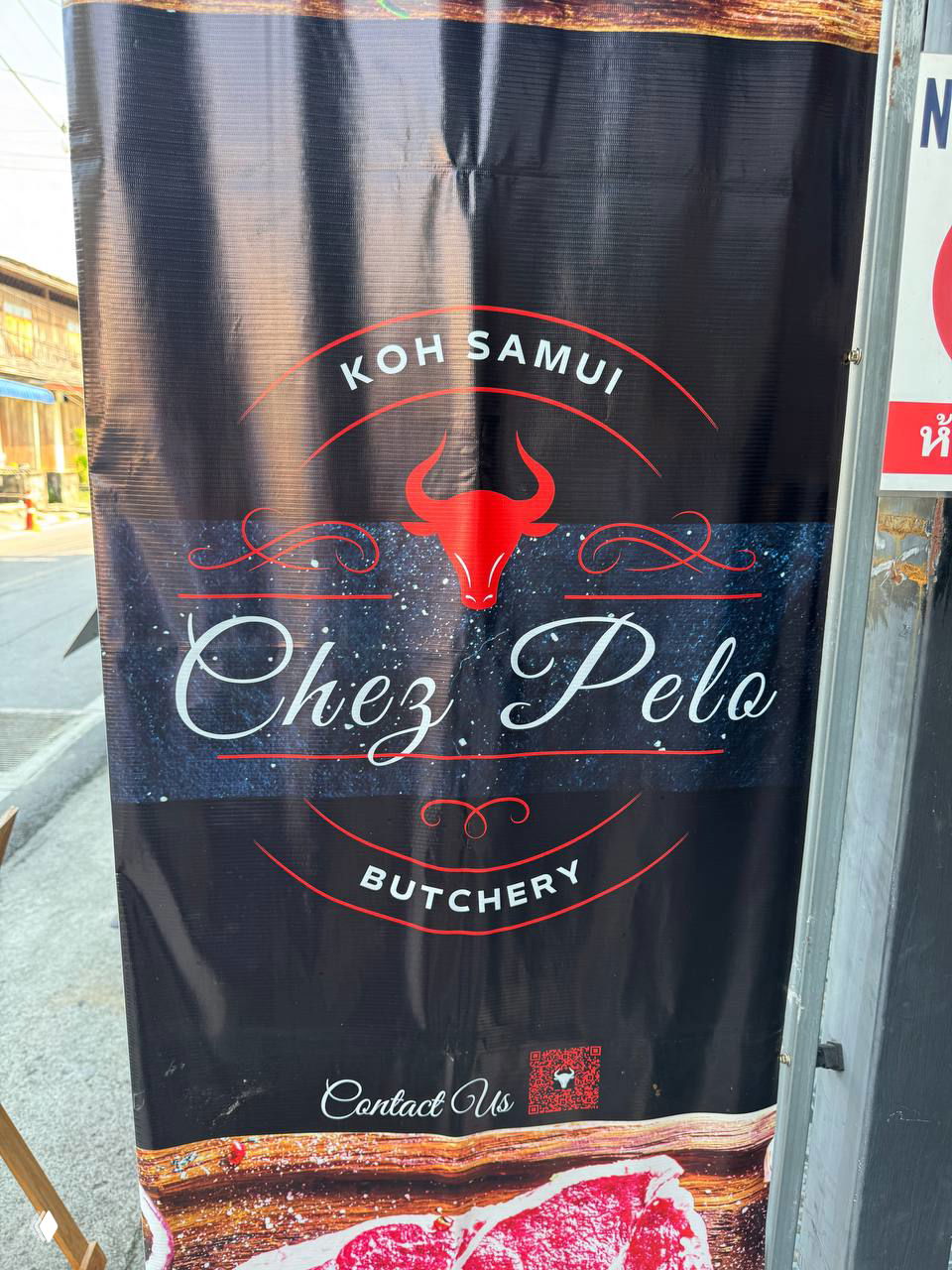 Уличный баннер с надписью Koh Samui Chez Pelo Butchery и изображением головы быка — рекламный плакат мясной лавки на улице Самуи.