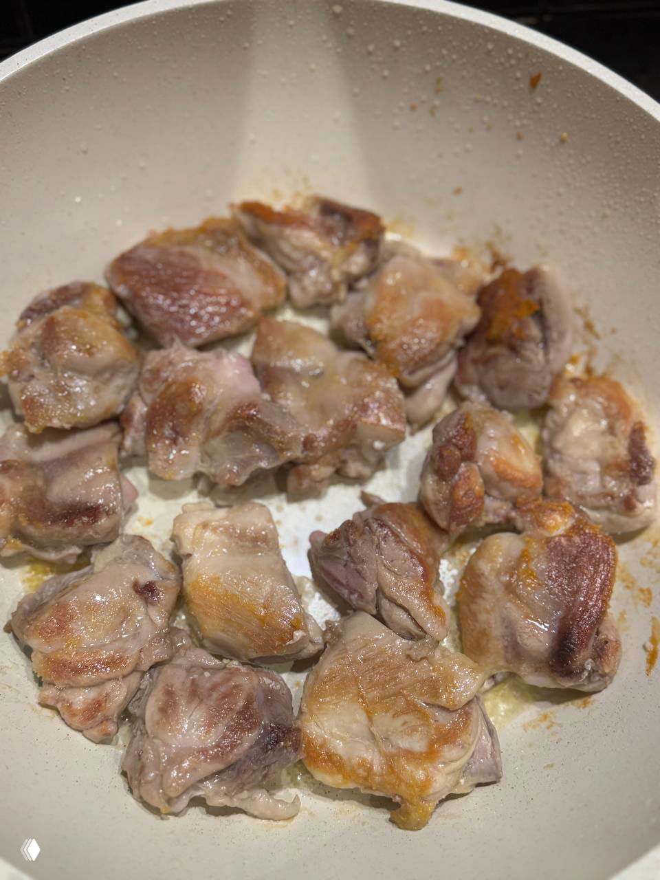 Кусочки курицы, обжаренные до золотистой корочки в белой сковороде, видно текстуру и степень прожарки крупным планом.