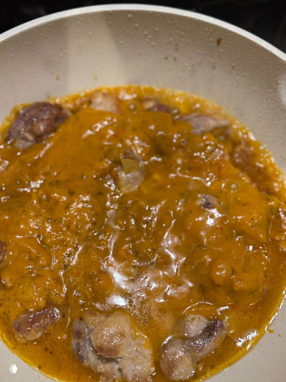 Кусочки курицы в сковороде, залитые оранжевым соусом Butter Chicken, видно консистенцию соуса и процесс тушения.