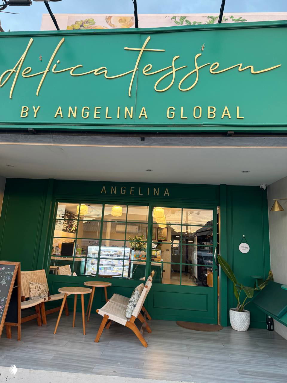 Фасад магазина Delicatessen by Angelina Global с зелёной вывеской, входная зона с креслами и столиками, вид с улицы и атмосферой небольшого бутика.