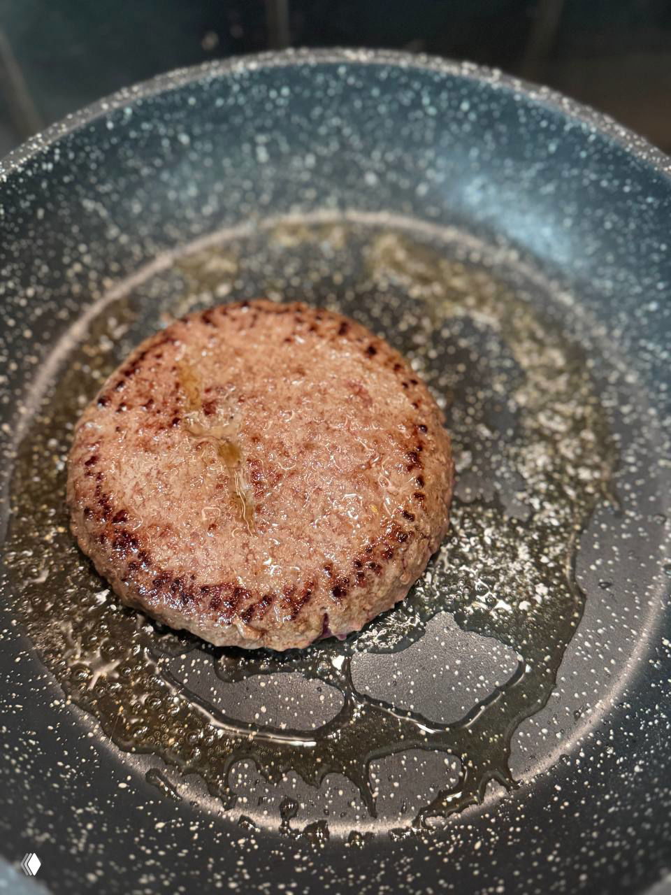 Котлетка из замороженного бургера жарится на сковороде в масле, видна корочка и горячее шипение, демонстрация процесса приготовления.