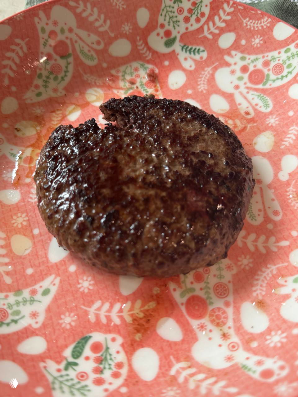 Готовая жареная котлета Marri Wagyu на розовой декоративной тарелке с узором, видна потёртая корочка и след масла после жарки.