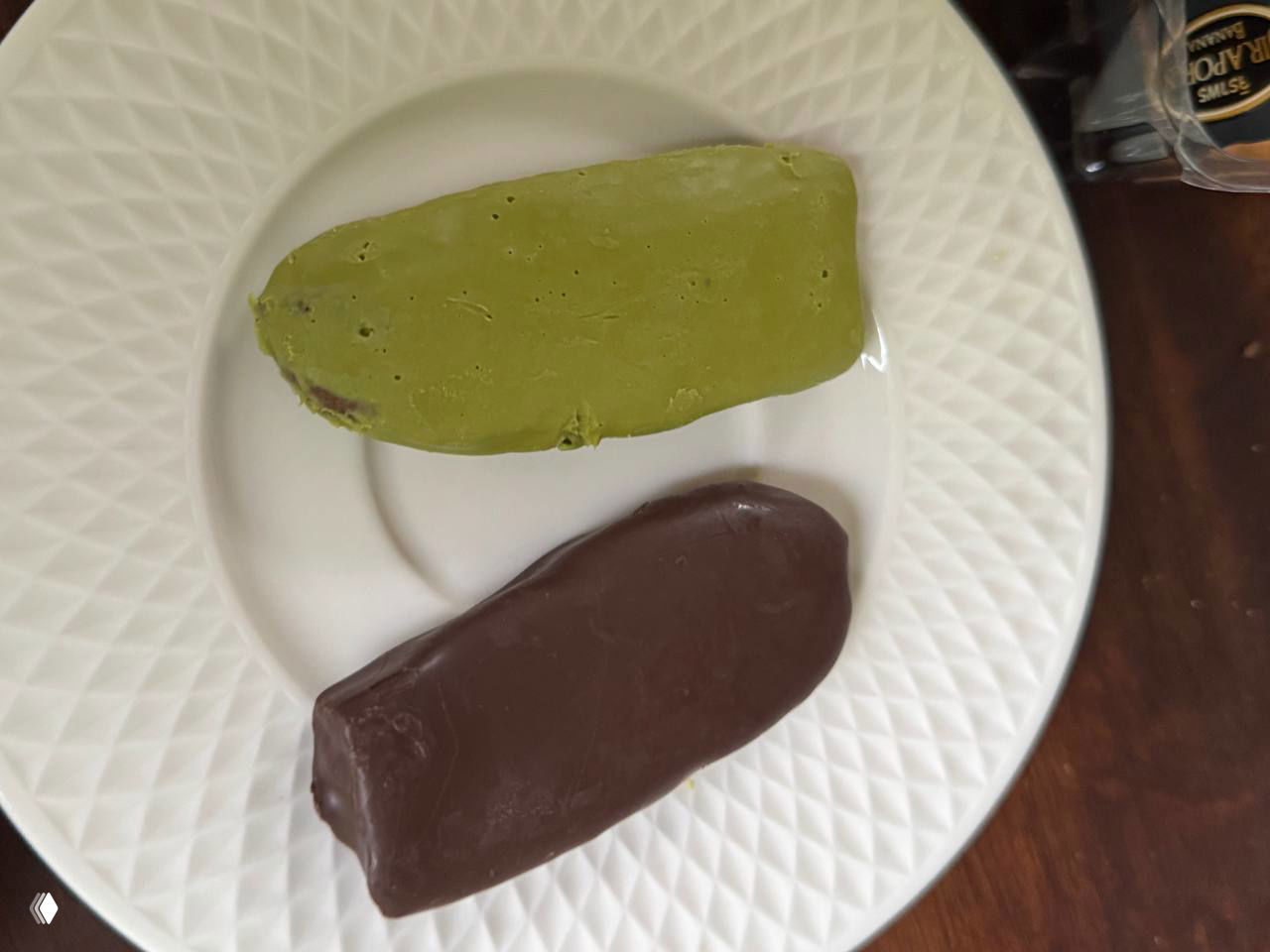 Две сушёные банановые пластинки на белой тарелке: одна покрыта глазурью зелёного чая, другая — шоколадом; крупный план, видно текстуру и покрытие.