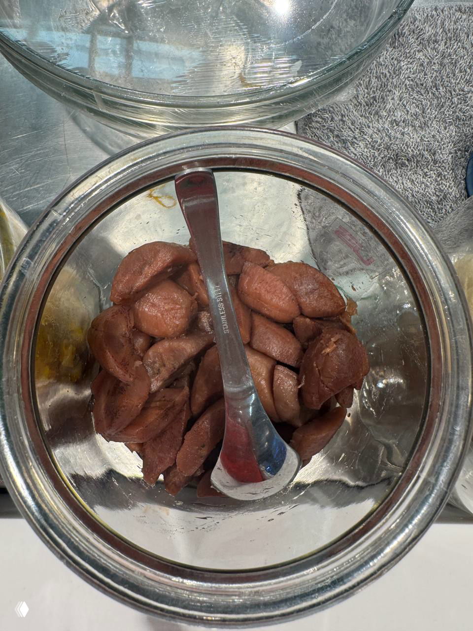 Стеклянная банка с коричневыми кусочками (батат или сладкий картофель), вид сверху, ложка и металлическая поверхность прилавка