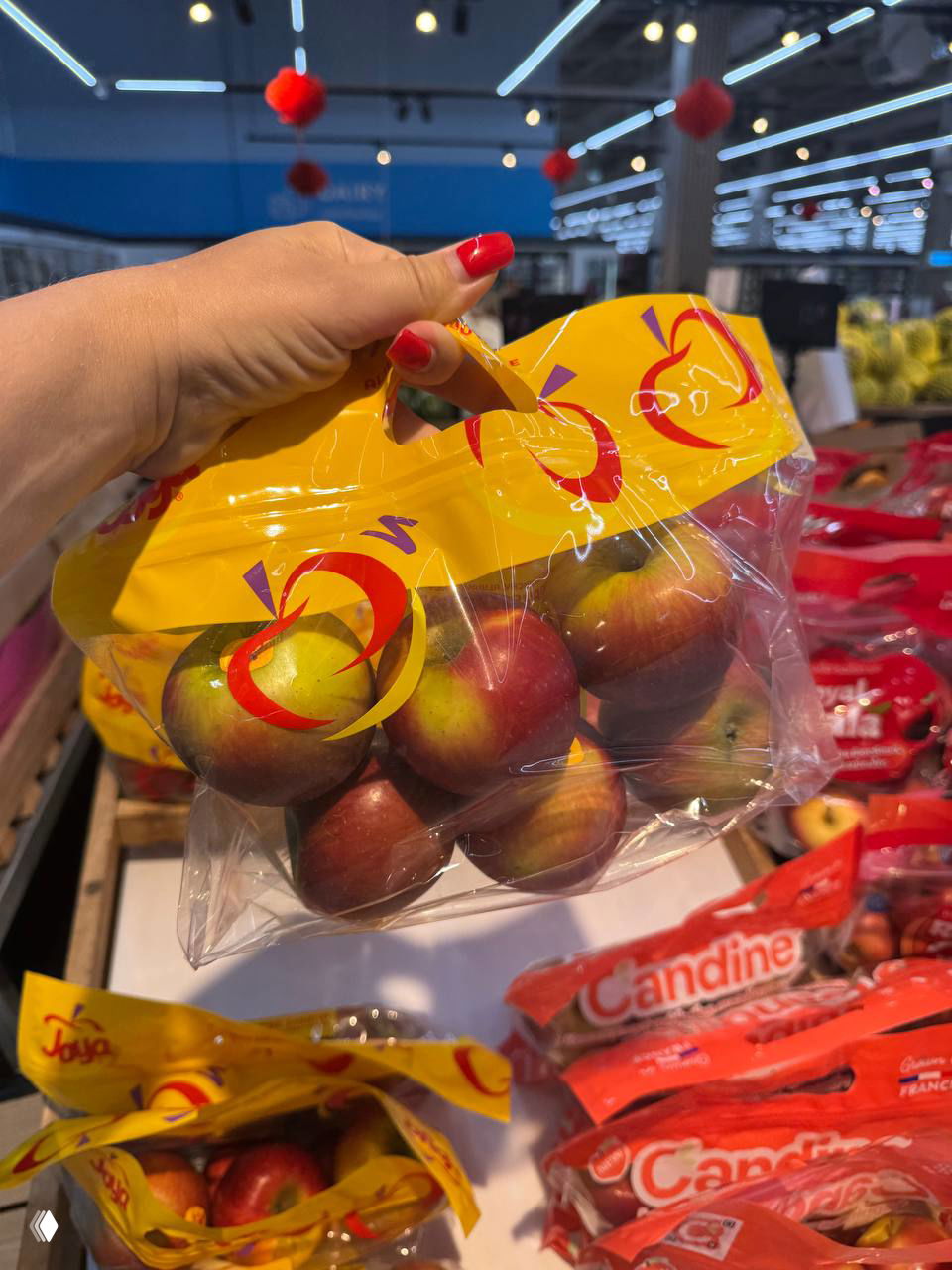 Прозрачный пакет с яблоками в жёлтой упаковке на витрине супермаркета Lotus; видны соседние фрукты и ценник 99 батт.