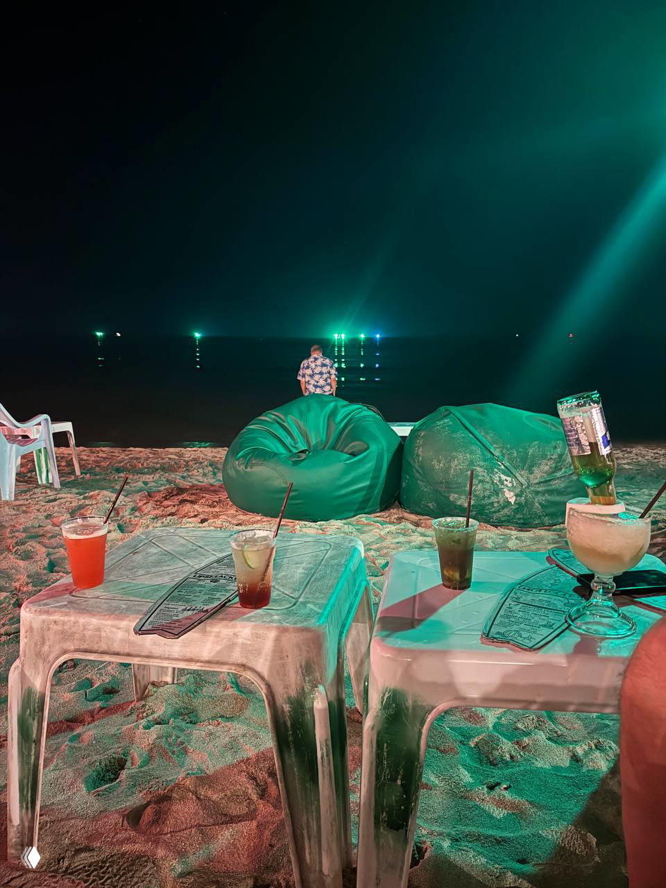 Вид с места на море: бинбэги и столики на песке с коктейлями, ночные огни в море и спокойная пляжная атмосфера на Чавенге.