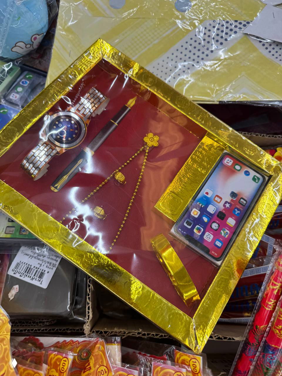 Упаковка с бумажными подношениями — миниатюрные имитации часов, украшений и смартфона, обёрнутые в золотую фольгу на витрине рынка.