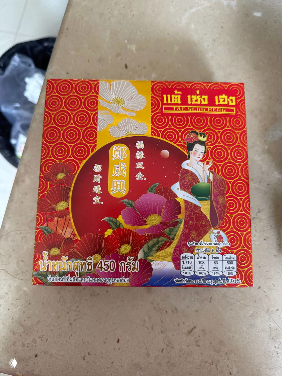 Упаковка mooncake: красная декоративная коробка с азиатскими орнаментами и надписями, на столе видна маркировка веса и яркий рисунок.