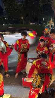 Группа барабанщиков в ярко‑красных костюмах исполняет ритм львиного танца на открытой площадке рядом с дорогой в Чайна таун Самуи.