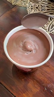 Открытая банка шоколадного мороженого крупным планом: гладкая, шелковистая текстура поверхности с воронкой в центре, вид сверху.