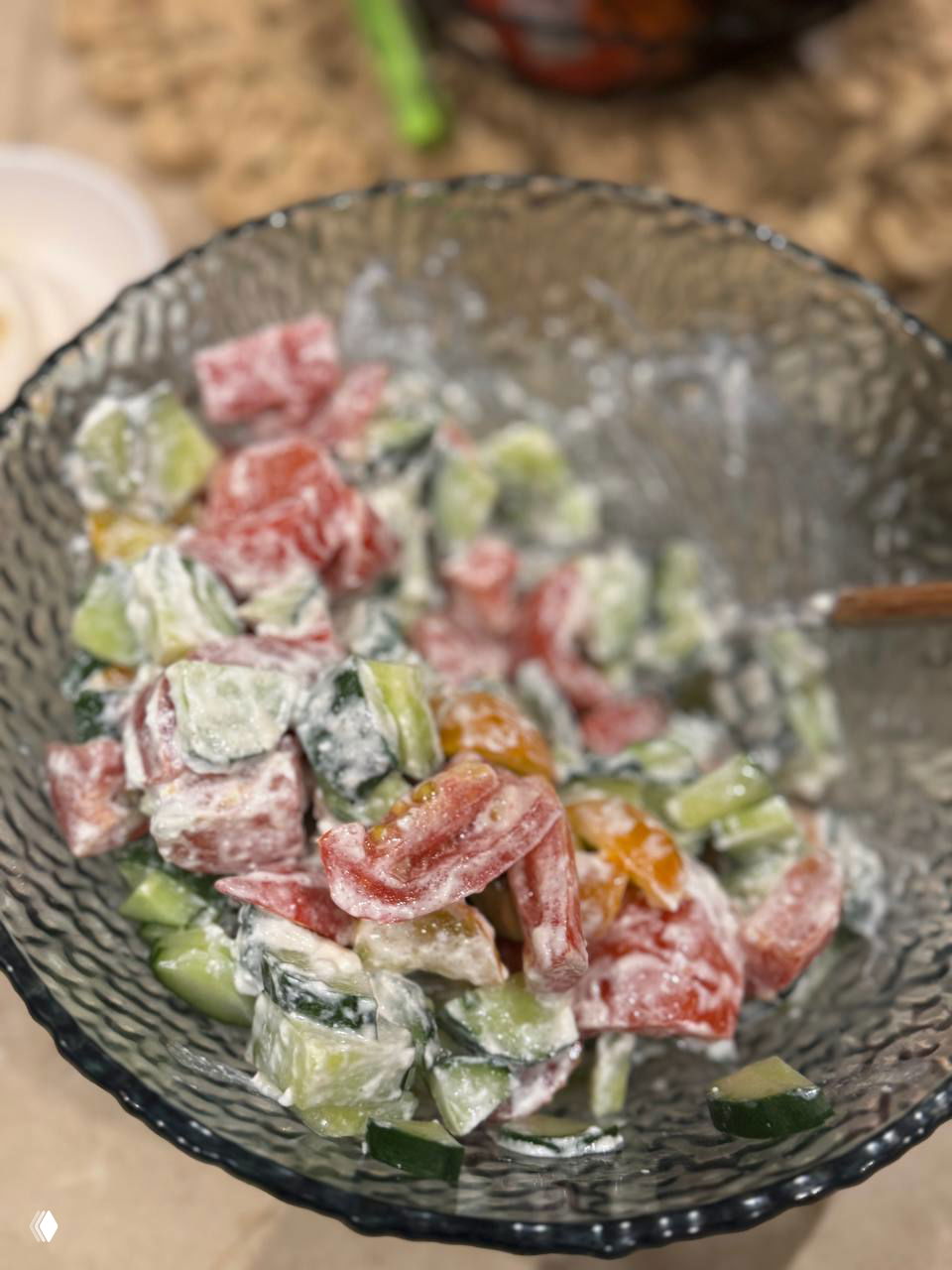 Салат в стеклянной миске с крупно порезанными огурцами и помидорами, заправленный сливочным или йогуртовым соусом, вид сверху.