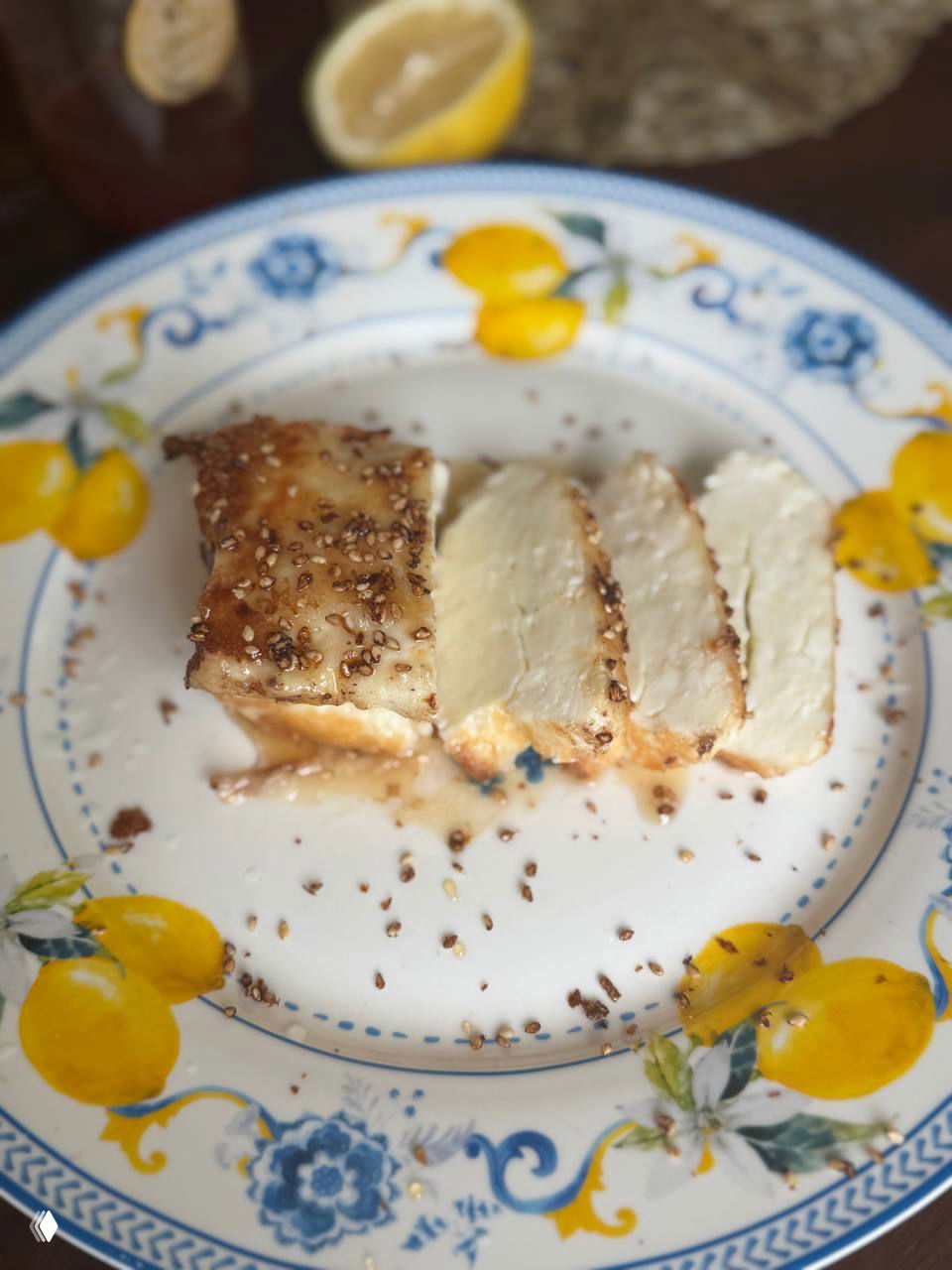 Нарезанный жареный халуми на тарелке с лимоном, мёдом и посыпкой кунжута — подача блюда на яркой лимонной тарелке.