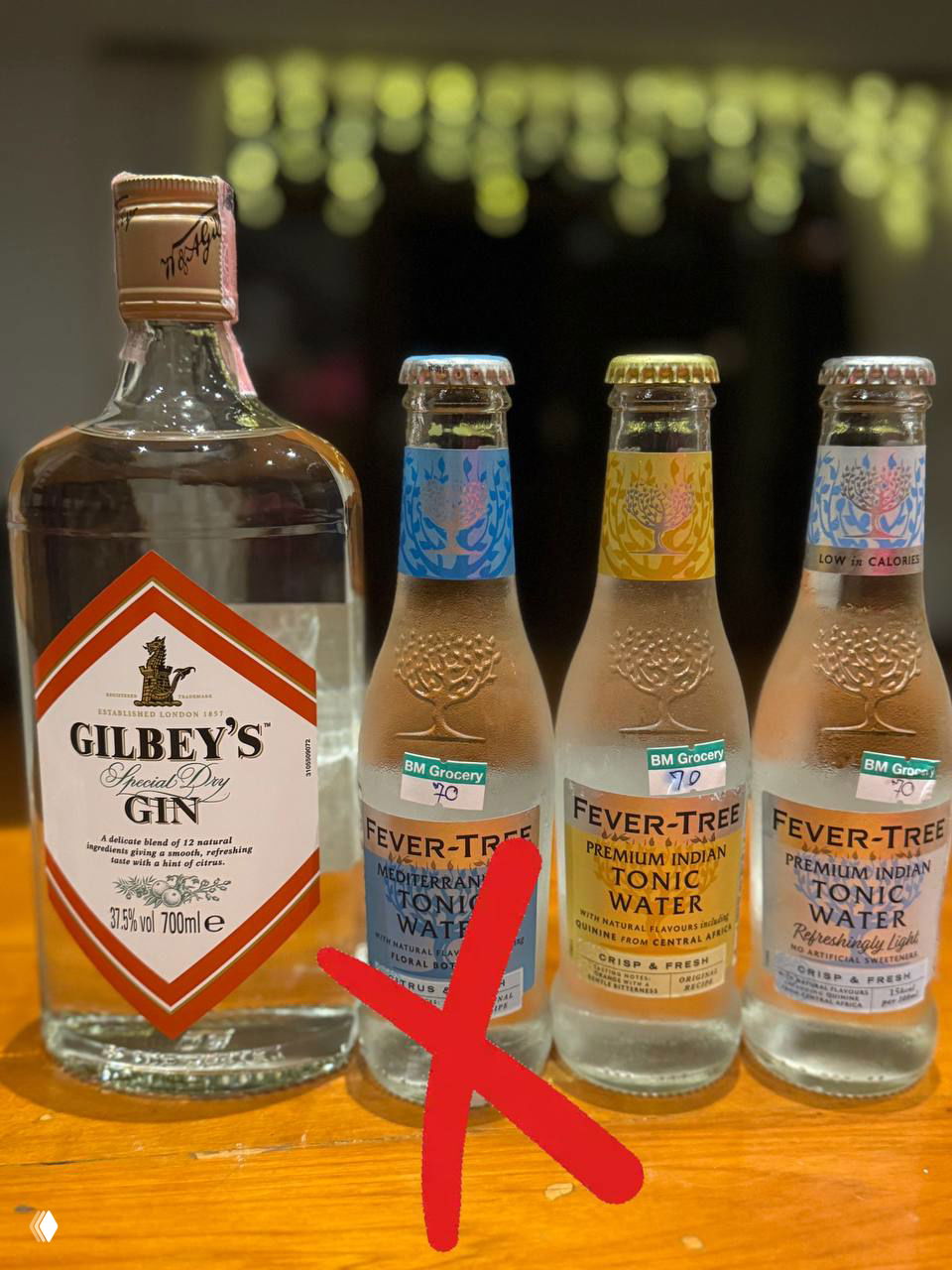 Бутылка Gilbey's и три бутылочки тоника Fever-Tree в ряд на барной стойке; крупный красный крест показывает, что сочетание не сработало по вкусу в эксперименте.