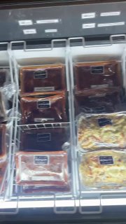 Холодильная витрина с несколькими контейнерами замороженных блюд La Guinguette, выставленных в лотках — вид в вертикальном кадре с полками.