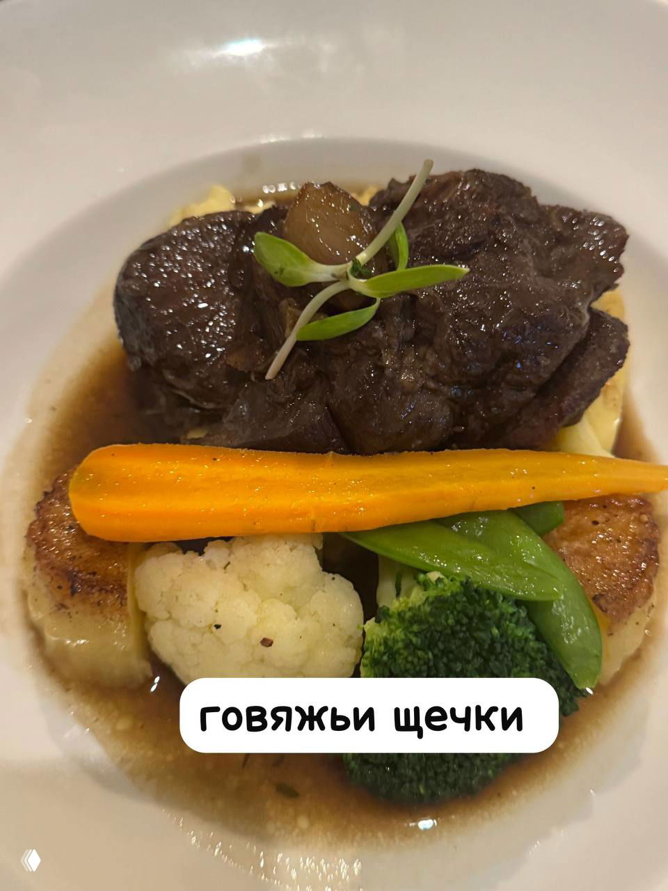 Главное блюдо — говяжьи щечки с глазированной морковью и гарниром из цветной капусты и брокколи, поданы на белой тарелке в Chez Francois.