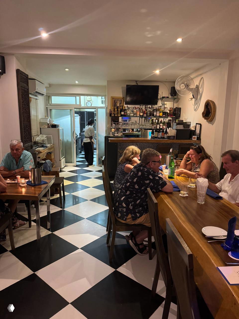 Вид интерьера первого этажа ресторана: чёрно‑белая плитка на полу, гости за столиками и барная зона — уютная домашняя атмосфера заведения.