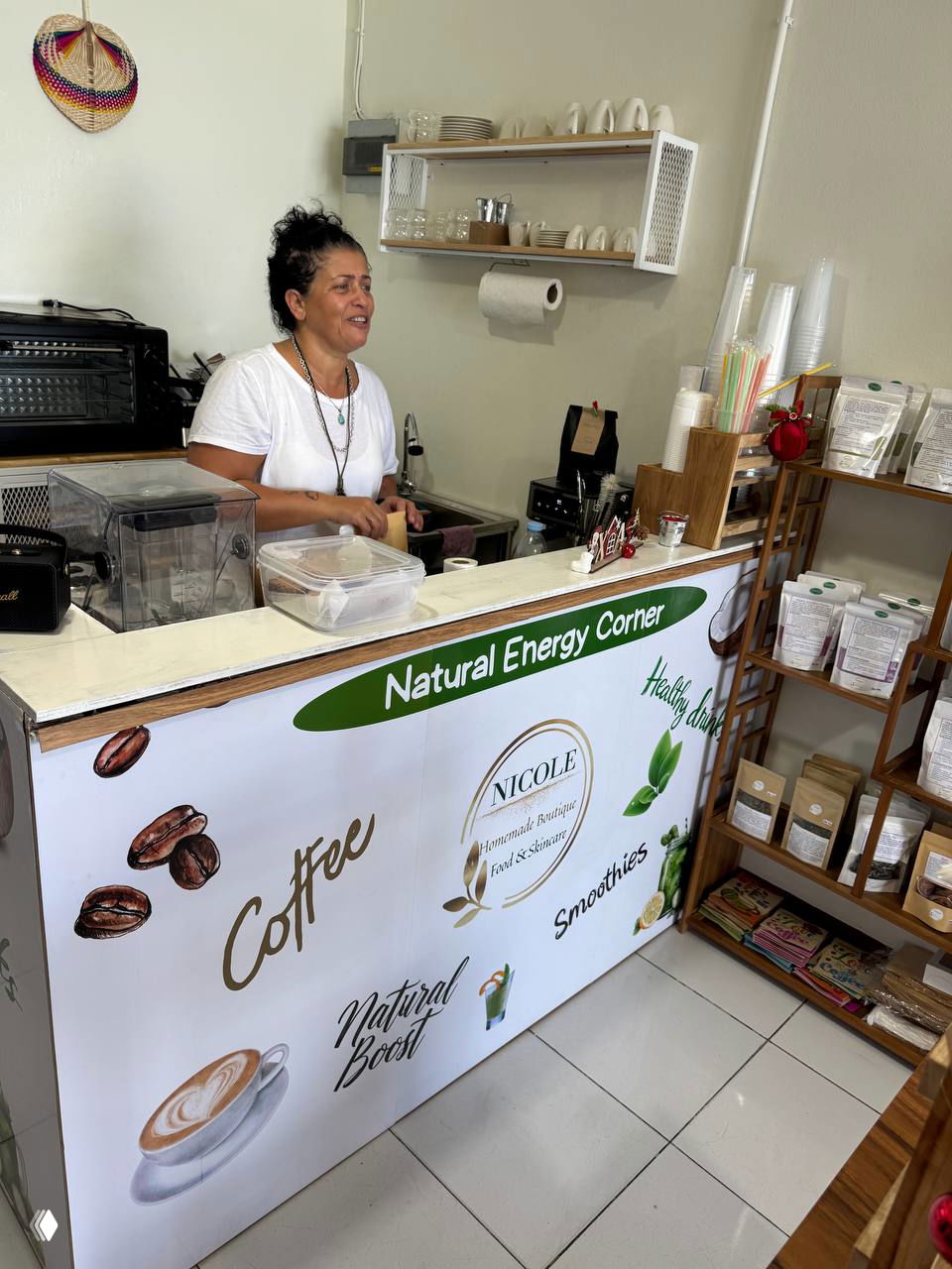 Прилавок магазина с надписью Natural Energy Corner и сотрудницей за стойкой, видны кофемашина, пакеты с товарами и бренд Nicole.