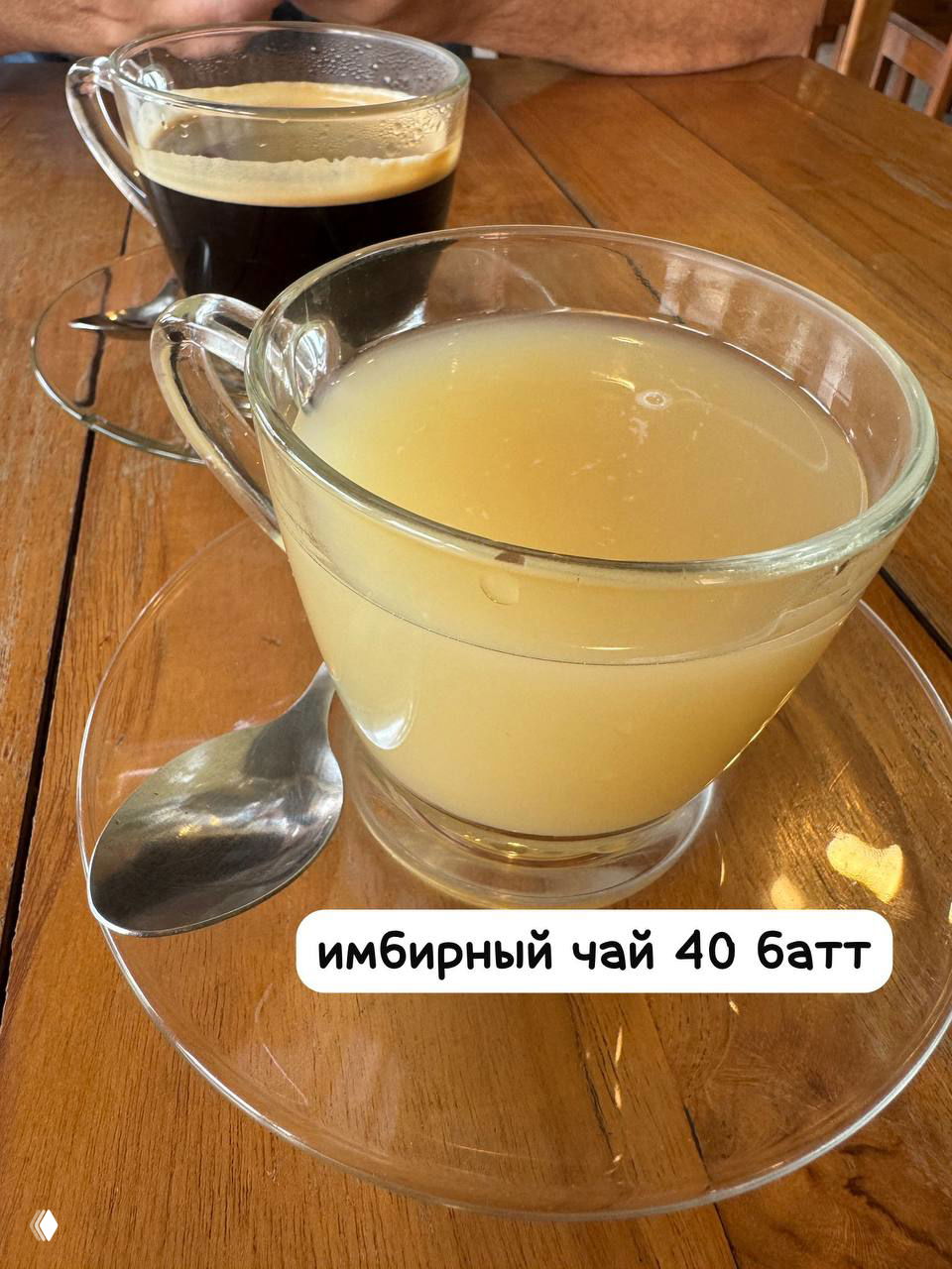 Две прозрачные чашки: имбирный чай цвета янтаря и чашка чёрного кофе на деревянном столе со столовой ложкой, подача в кафе.