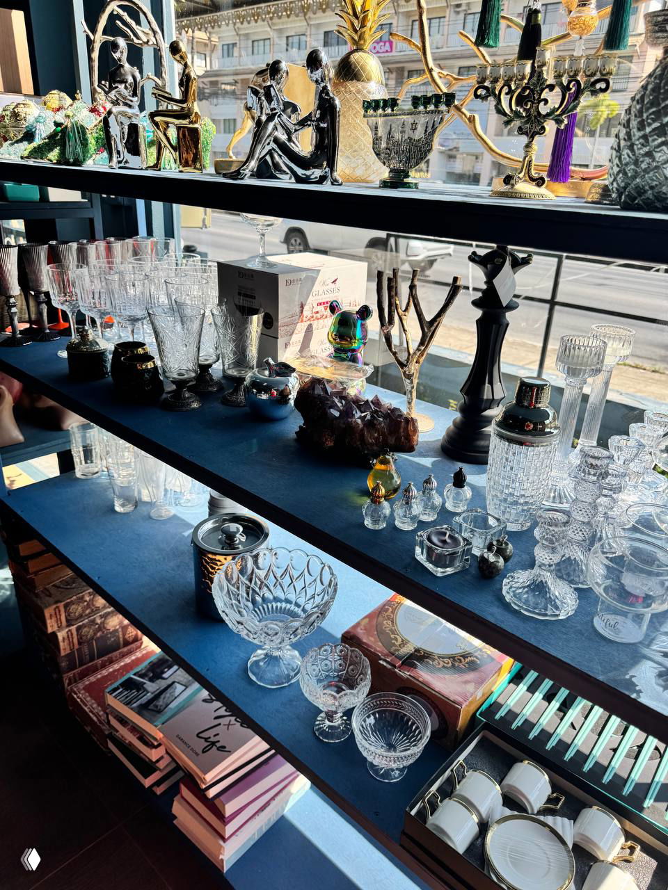 Стеллаж с разнообразным стеклянным и хрустальным сервизом: бокалы, вазы и пиалы выставлены у витрины магазина подарков на Самуи, много отражений и света.