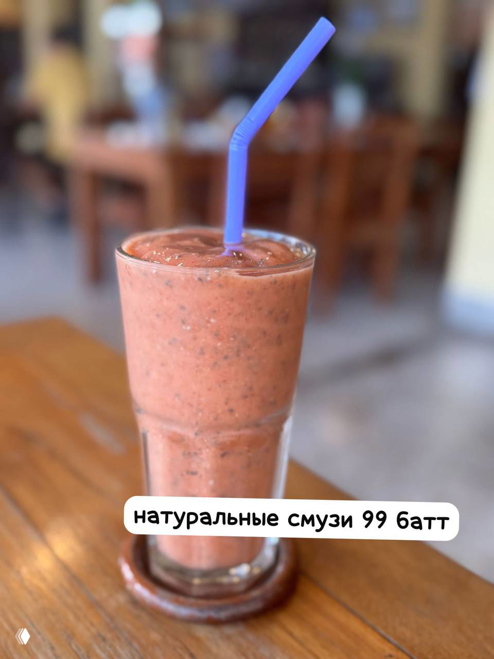 Высокий стакан с розовато-коричневым смузи и фиолетовой трубочкой на столе, фоново размытая часть зала кафе, свежая подача.