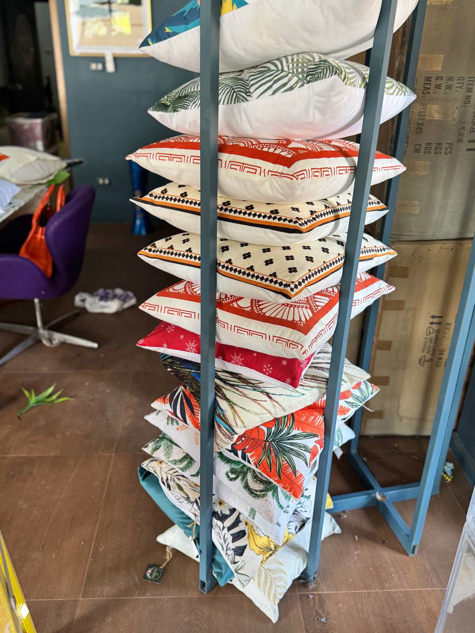 Высокая стойка со стопкой декоративных подушек и наволочек разного принта и цвета — текстиль для дома и подушки, выставленные в магазине подарков на Самуи.