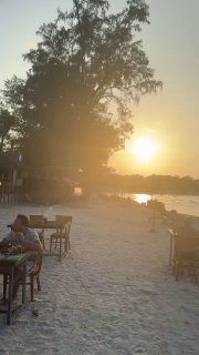 Пляжная аллея и расставленные столики у воды в Pi beach club на Самуи во время золотого часа, силуэты гостей на берегу.