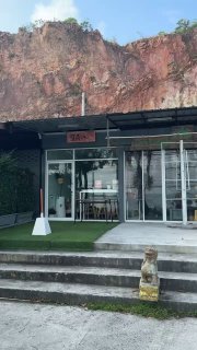 Вход в Golden Crust на фоне внушительной скалы: небольшая терраса и фасад кафе рядом со строительной площадкой.