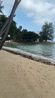 Песчаный пляж Ламая с мелкой прибрежной линией, пальмами и спокойным морем при облачной погоде, вид по диагонали на берег.