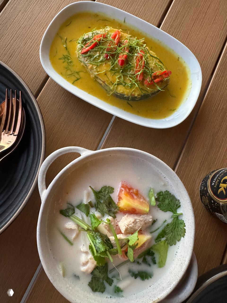 Тарелка с карри и тарелка с тайским супом том-ям на деревянном столе — примеры блюд из меню ресторана Sora Sierra.