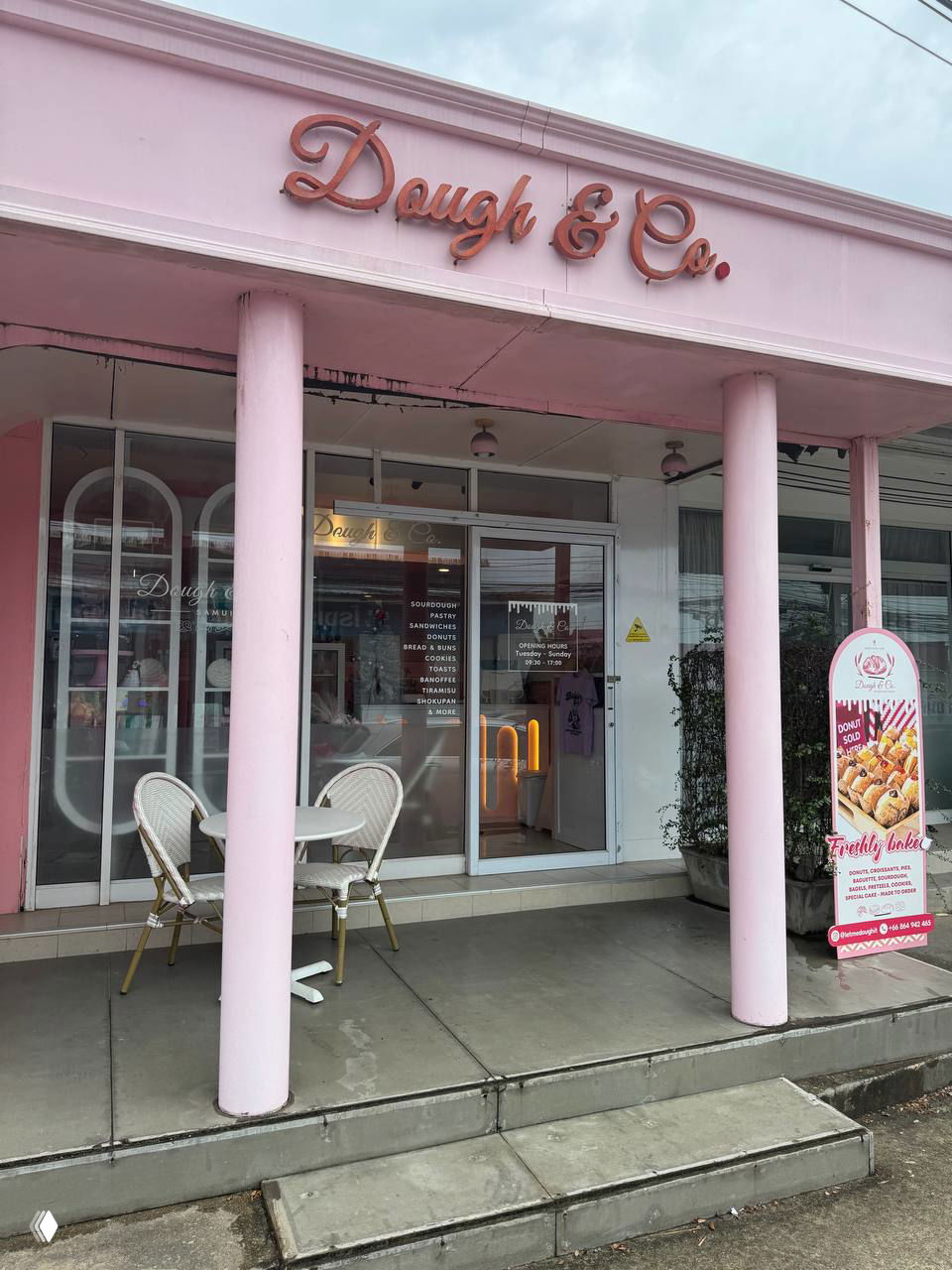 Фасад розового магазина Dough & Co на Самуи: вход с колоннами, вывеска и уличная табличка с изображением пончиков, наружная обстановка.