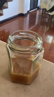 Небольшая стеклянная банка с жидким коричневым медом безжальных пчёл на деревянной поверхности в домашнем интерьере; объём небольшой.