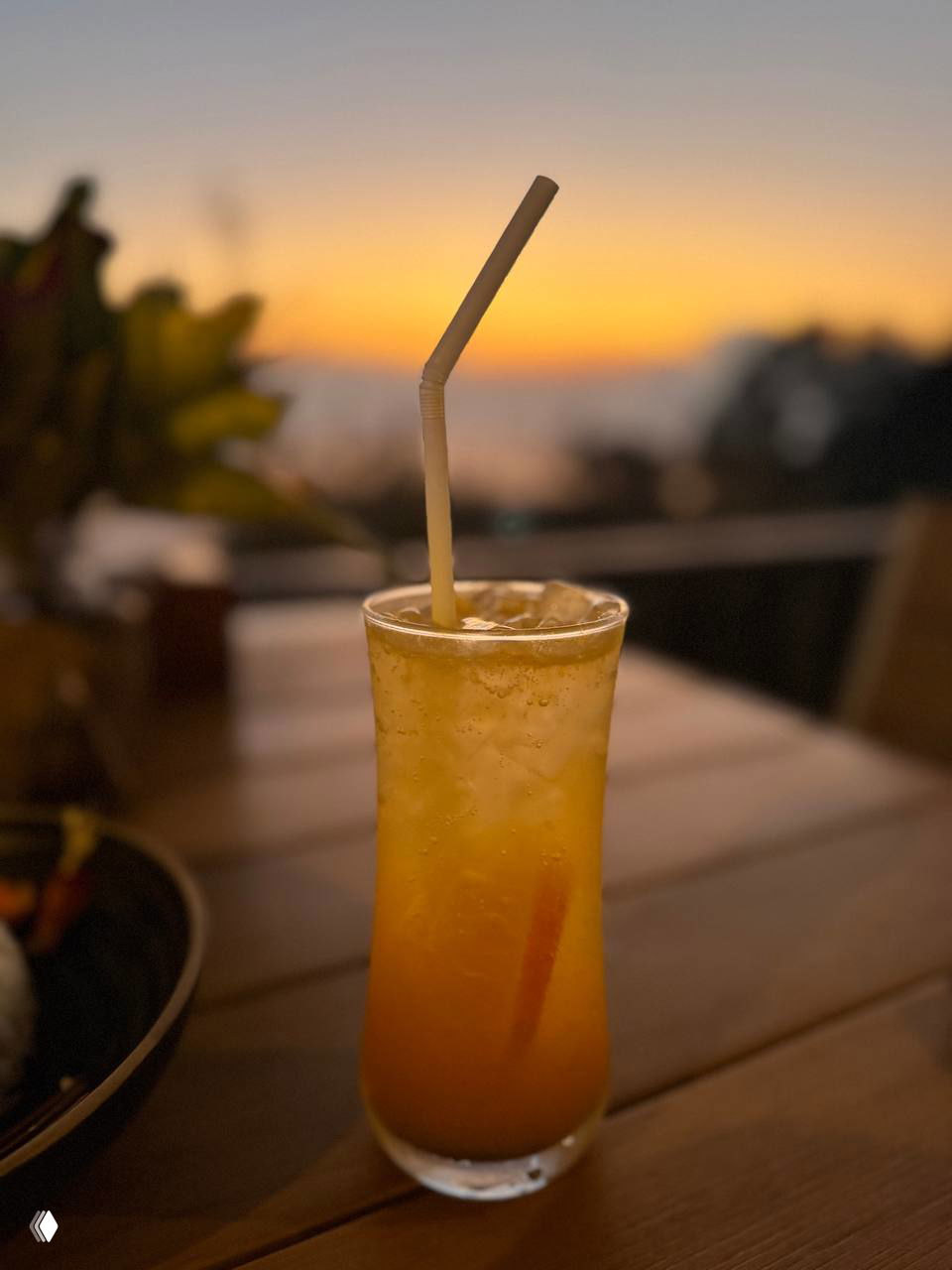 Стеклянный высокй стакан с апельсиновым моктейлем на фоне размытых сумерек — один из сбалансированных напитков заведения.