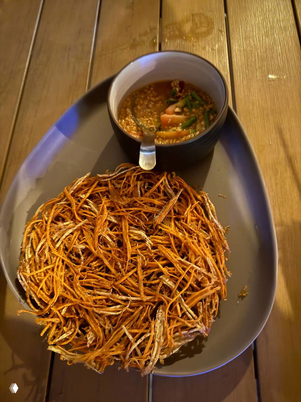 Блюдо с хрустящей корочкой и соусом в небольшой пиале — блюдо с яркой текстурой, поданное на темной тарелке.