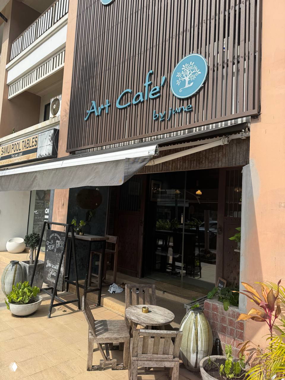 Фасад Art Cafe by June с бирюзовой вывеской, наружной террасой и столиками; у входа видно правило снимать обувь.